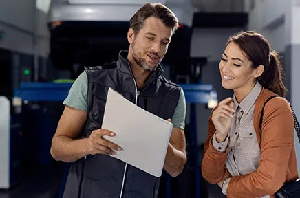 Ein Mann und eine Frau betrachten gemeinsam ein Dokument in einer modernen Werkstatt oder Produktionsumgebung und lächeln dabei.