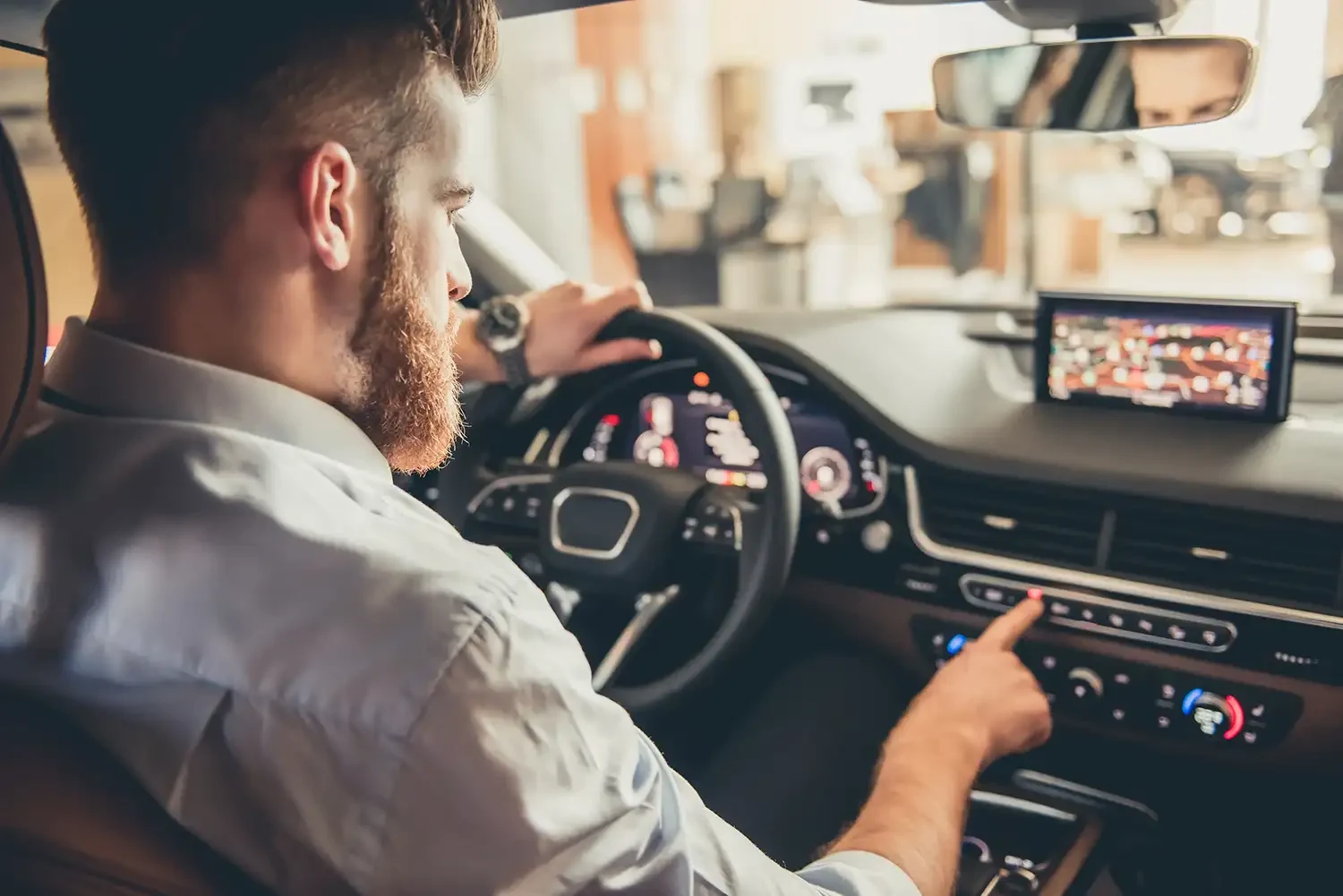 ein mann mit bart sitzt am steuer eines modernen autos und bedient das infotainmentsystem.