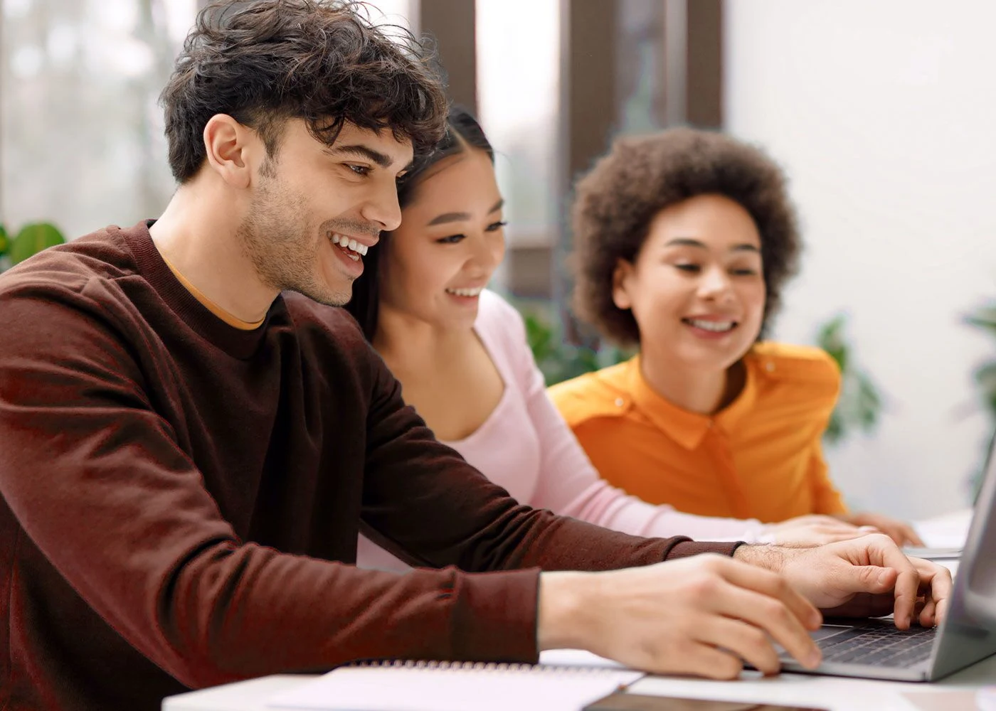 Eine Frau und ein Mann sitzen an einem Tisch mit Laptop und unterhalten sich in entspannter Atmosphäre mit Pflanzen im Hintergrund.