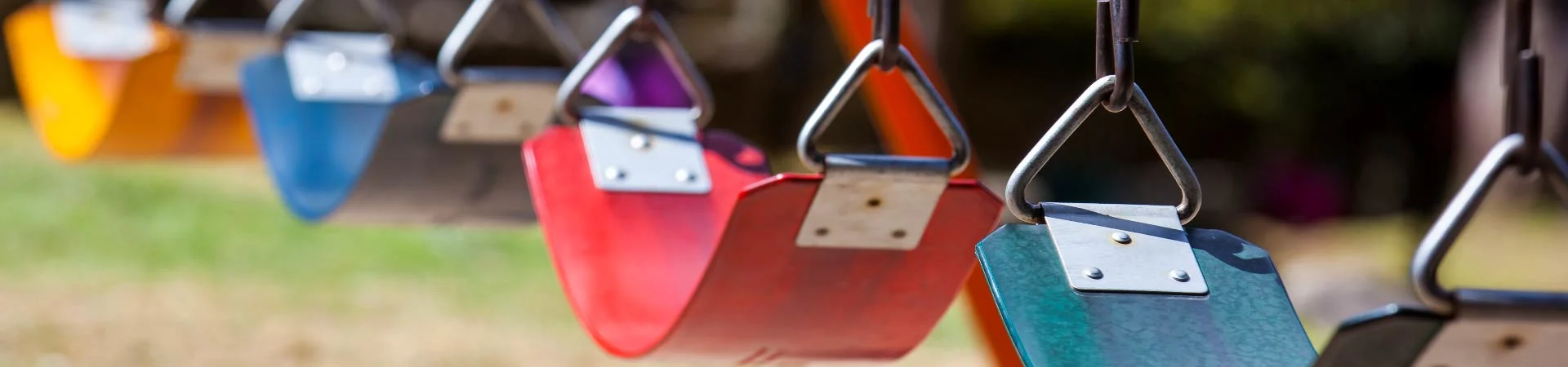 Bunte Schaukelschalen in Rot, Blau und Orange an Metallketten auf einem Spielplatz, mit unscharfem Hintergrund.