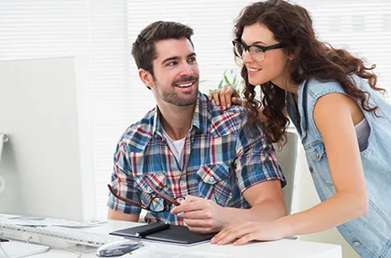 Zwei junge Kreative arbeiten gemeinsam an einem Computer mit Grafiktablett in einem hellen, modernen Büro.