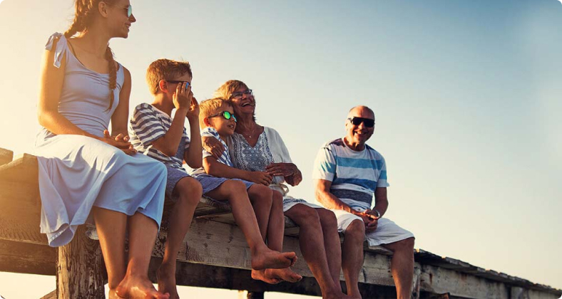 Familie sitzt auf einem Steg und genießt den sommerlichen Sonnenuntergang. 