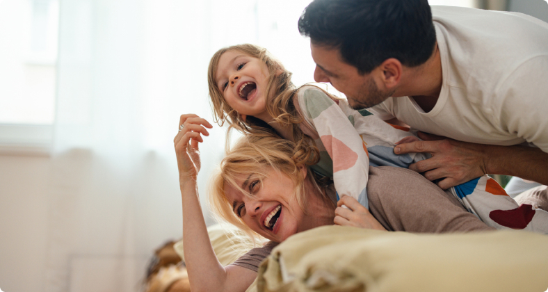 Glückliche Familie spielt zusammen mit ihrem Kind auf dem Bett.