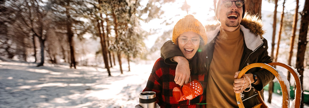 Glückliches junges Paar läuft mit einem Schlitten durch den winterlichen Wald.