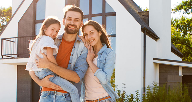 Junge Famile steht glücklich vor ihrem Haus.