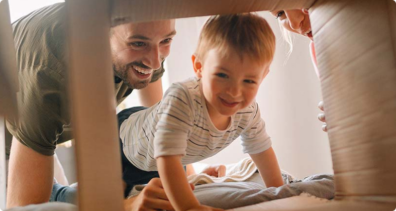 Mutter und Vater spielen mit ihrem Kleinkind unter einem Pappkarton.