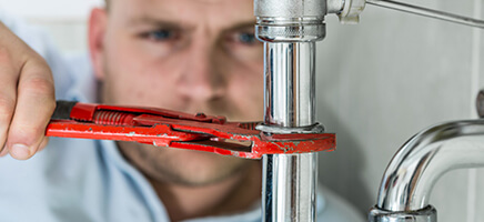 Ein Handwerker arbeitet mit der Wasserpumpenzange an einem Sifon unter dem Waschbecken.