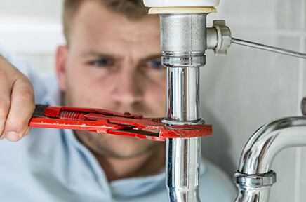 Ein Handwerker arbeitet mit der Wasserpumpenzange an einem Sifon unter dem Waschbecken.