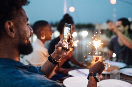 Ein Mann filmt eine Gartenparty mit seinem Handy.