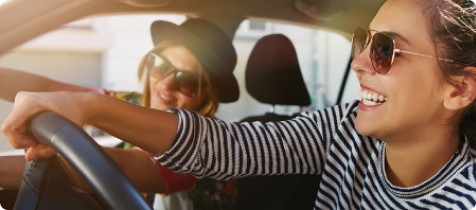 Zwei junge Frauen sitzen lachend in ihrem Auto.